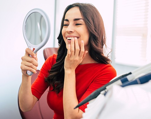 Woman in red shirt checking her smile in a handheld mirror