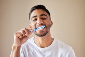 Man in white shirt smiling while brushing his teeth