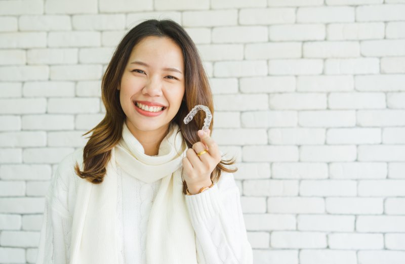 woman smiling and holding Invisalign aligner