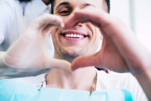 A smiling man and his dentist make a heart shape with their hands