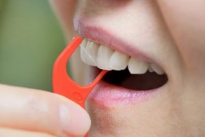 Someone using an orange, plastic flosser to clear the space between their teeth