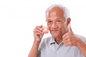 Older man holding pair of dentures and giving thumbs up.